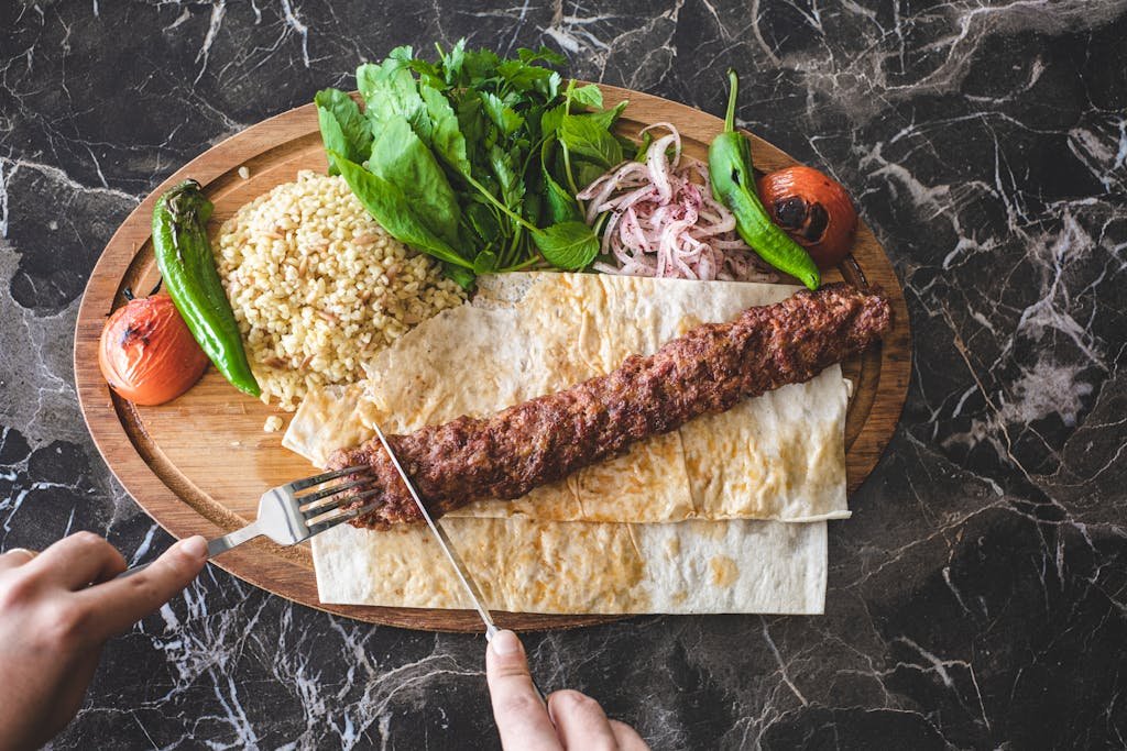 A mouthwatering Turkish kebab served with fresh vegetables and bulgur on a wooden plate.