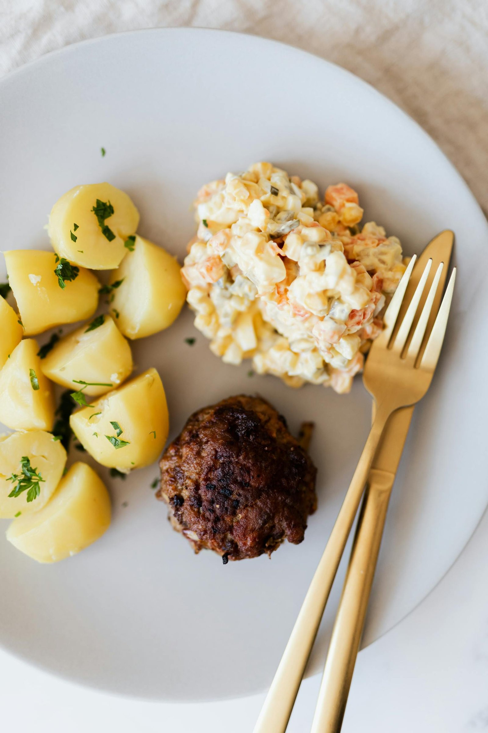 A savory plate featuring a tender meatball, boiled potatoes, and creamy salad.