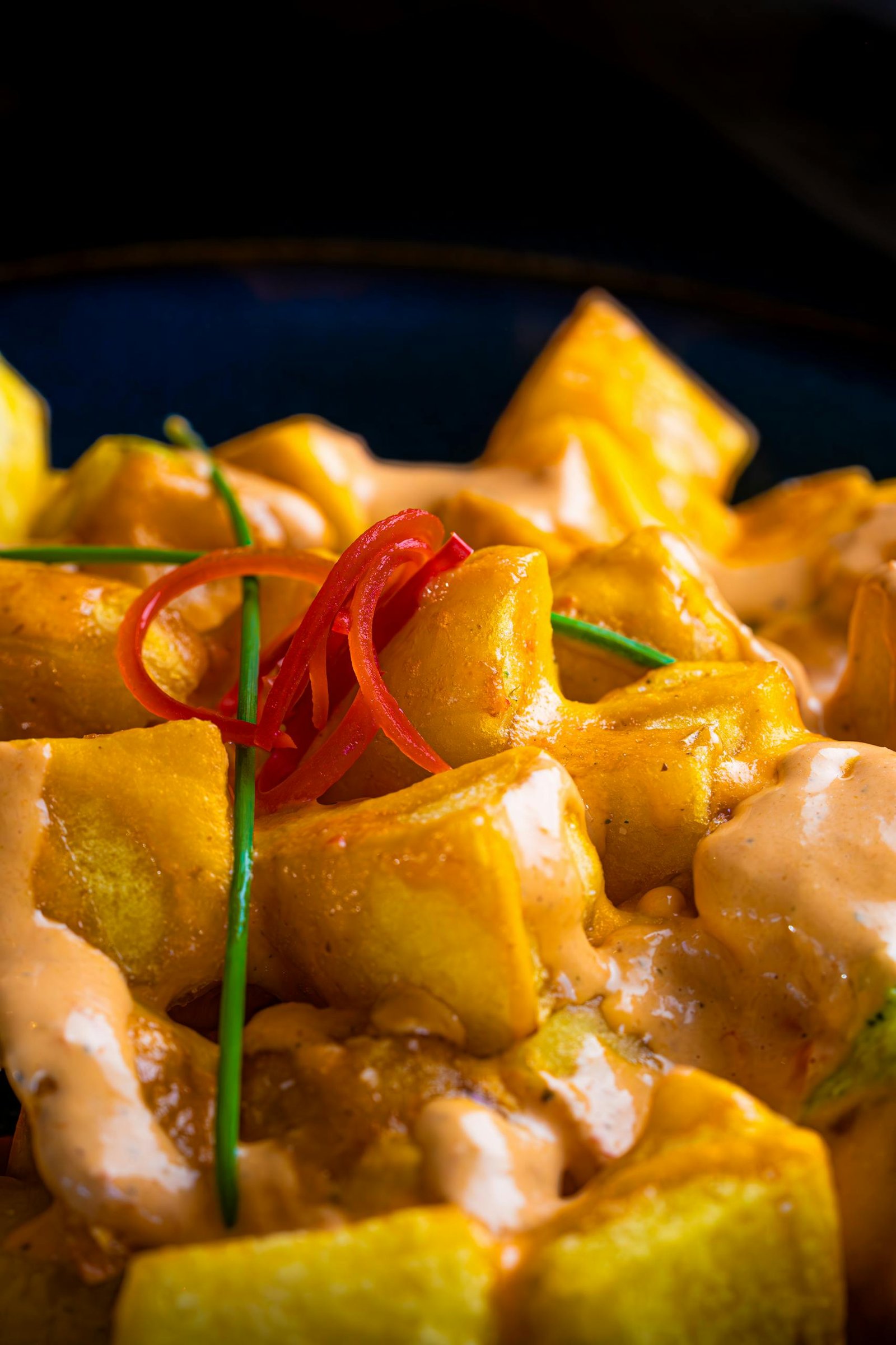 Spain Travel Guide: Things to know before travelling to Spain 15 Appetizing close-up of spicy patatas bravas with sauce, garnished with chives.