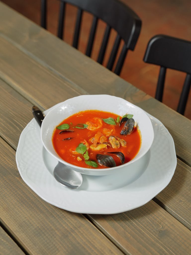 Delicious bouillabaisse seafood soup garnished with basil leaves, served in a white bowl on a wooden table.