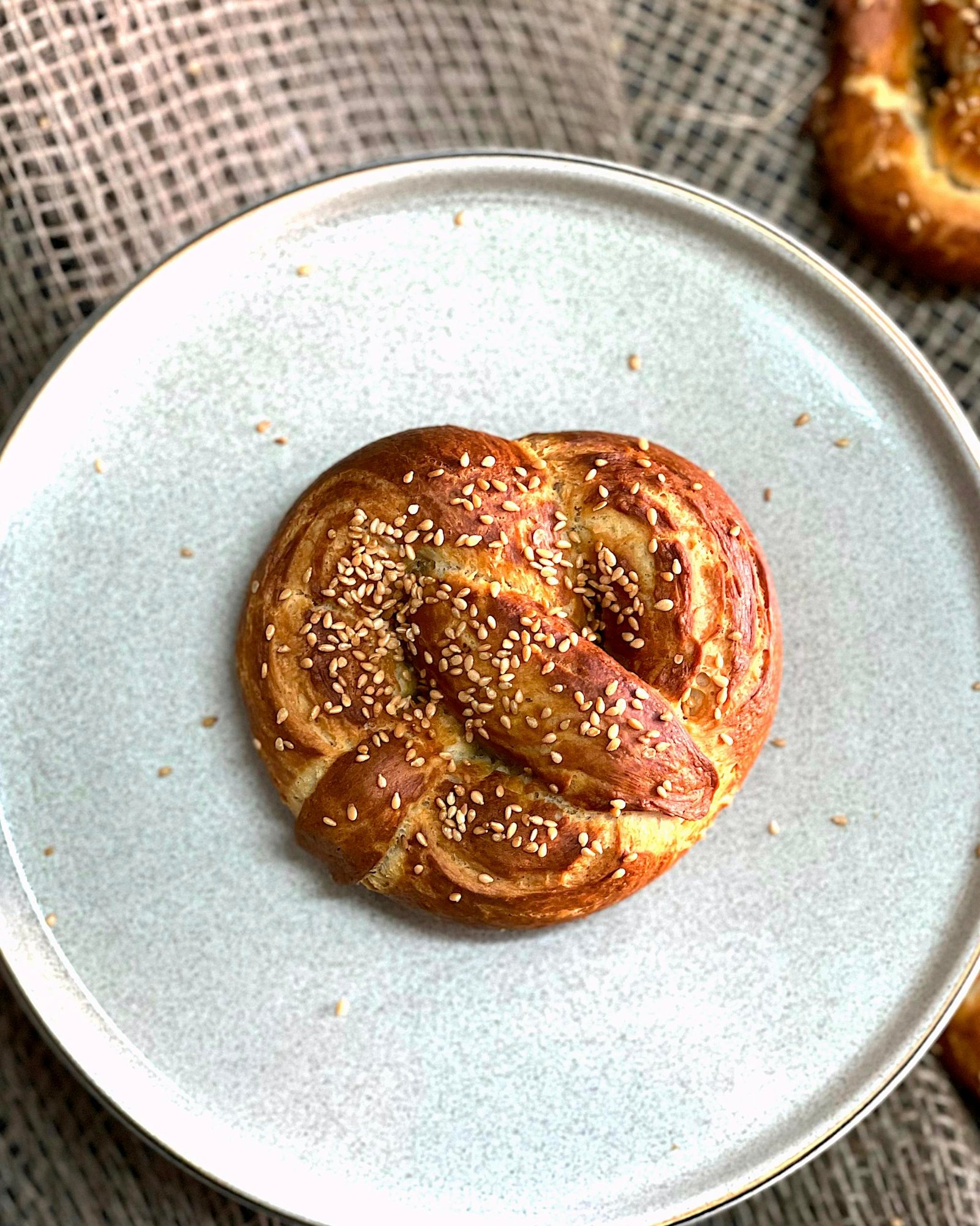 Golden brown pretzel topped with sesame seeds served on a white plate.