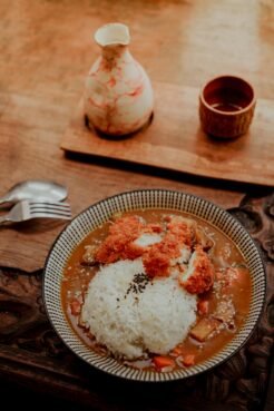Japan Travel Guide: Everything You Need to Know for an Unforgettable Trip 14 Japanese curry rice with breaded chicken served with sake set on a rustic wooden table.