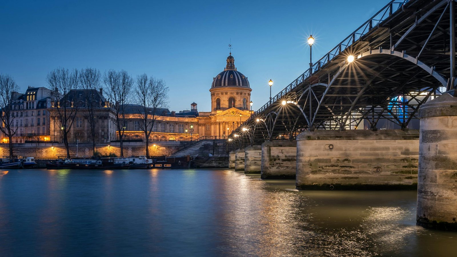 Scenic twilight view of Institut de France and Pont des Arts in Paris with reflections on the Seine River.