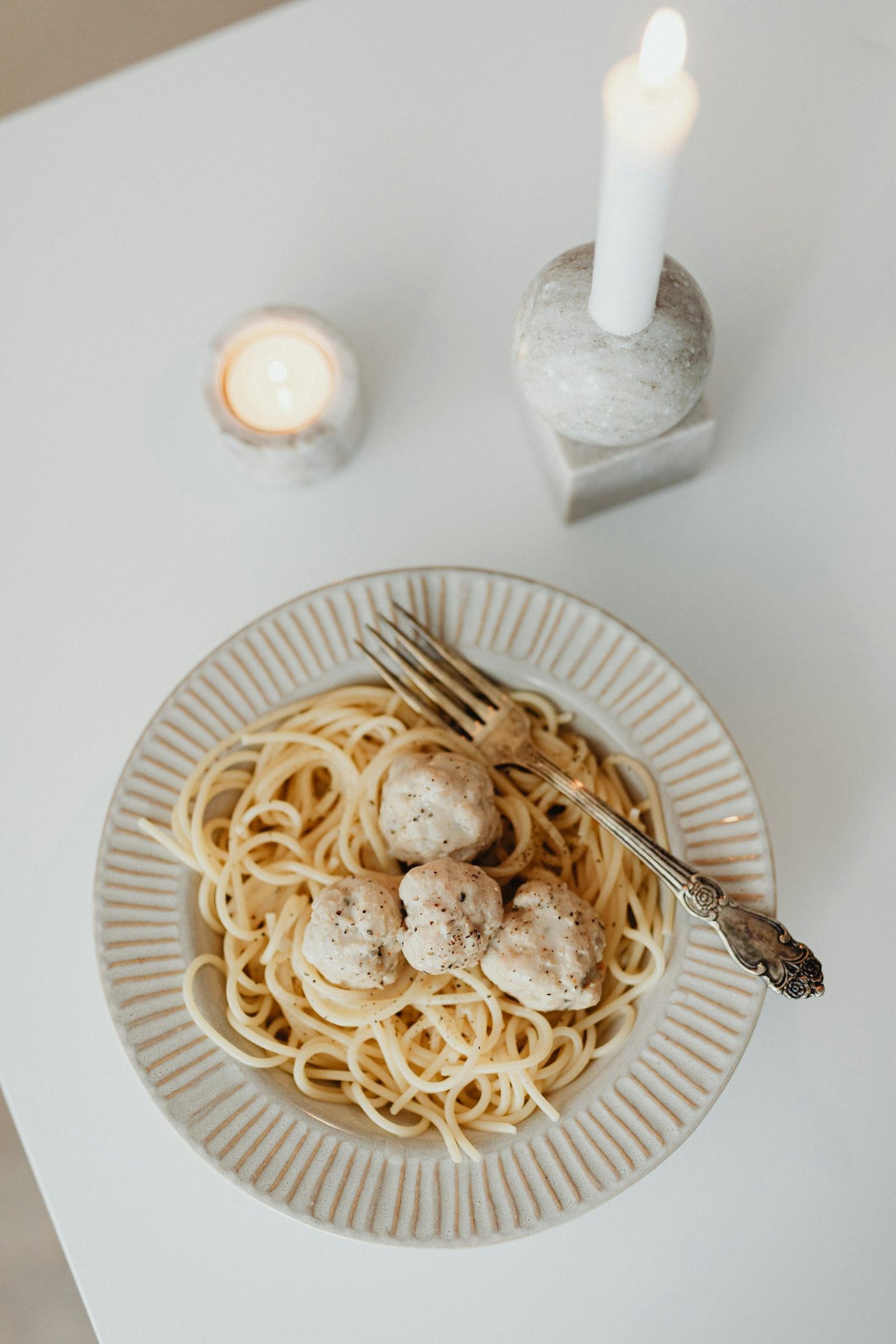 Tasty spaghetti and meatballs on a white plate, elegantly presented under candlelight.