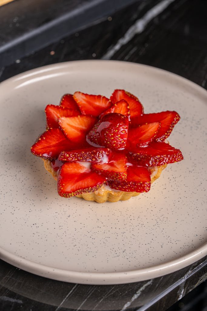 Close-up of a fresh strawberry tart beautifully arranged on a speckled ceramic plate.
