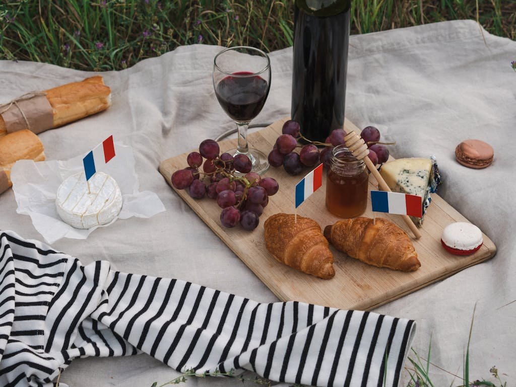 French food picnic with wine, croissants, and cheese on a cozy outdoor setup.