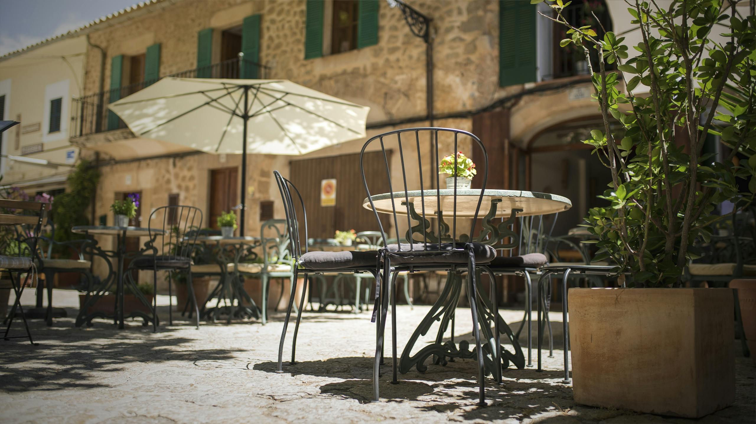Best Time to Visit Spain: A Complete Guide to Spain's Seasons and Weather 4 A quaint outdoor café in Mallorca, Spain, with iron chairs and rustic stone buildings.