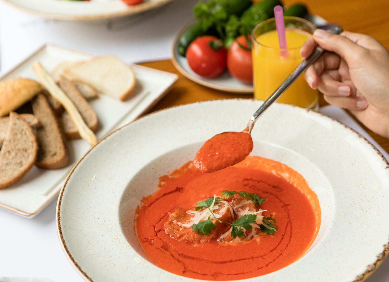 A savory tomato soup served with fresh bread and orange juice, perfect for a nutritious meal.