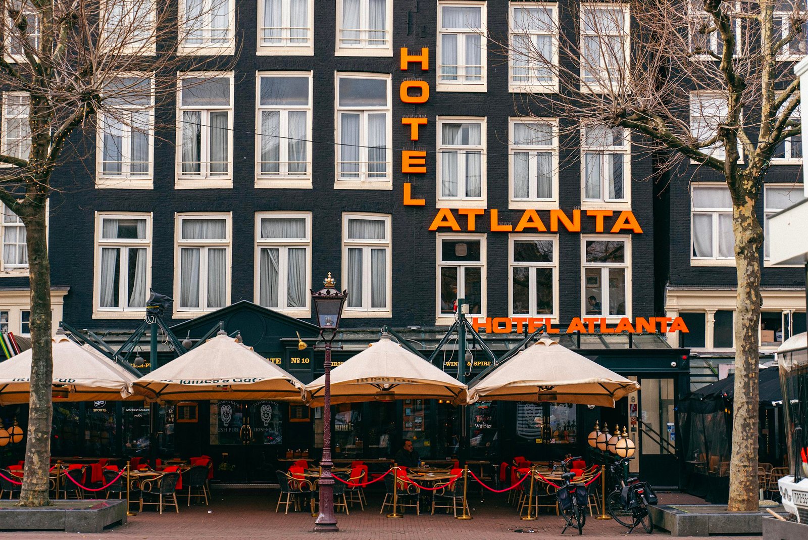 Facade of Hotel Atlanta in Amsterdam with outdoor cafe seating and umbrellas on a city street.