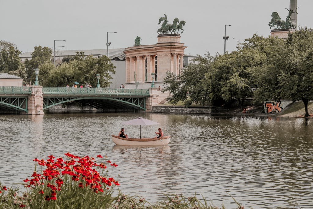 Peaceful scene of a boat on a calm lake near a historic bridge in Budapest.