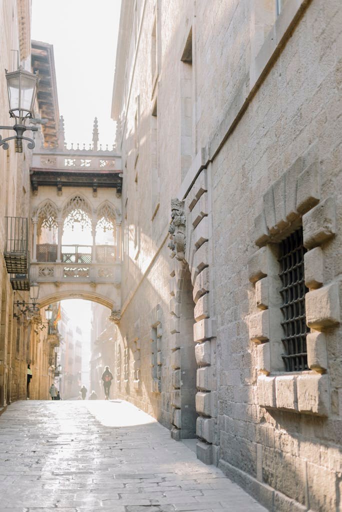Sunlit Gothic street with famous Bisbe Bridge in Barcelona's historic quarter.
