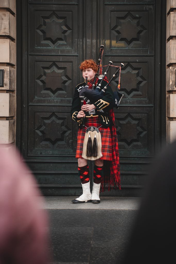45 Unique Things to Do in Edinburgh: Hidden Spots & Must-See Attractions 27 A traditional Scottish bagpiper in vibrant tartan attire stands before an ornate door in Edinburgh, Scotland.