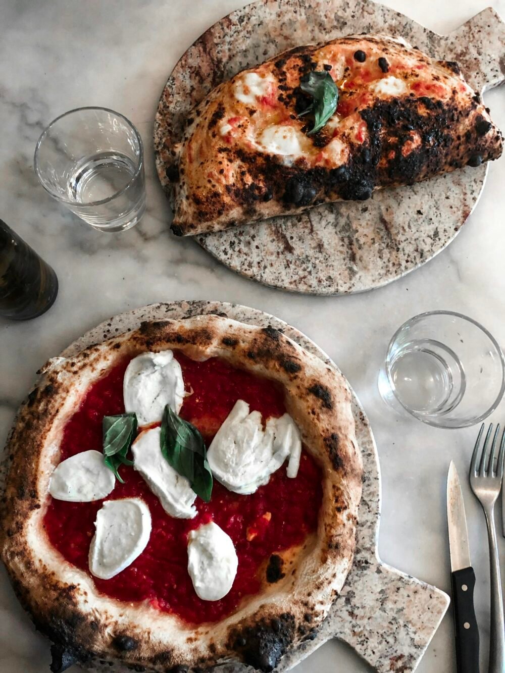 Close-up of artisan Neapolitan pizzas with fresh mozzarella and basil, styled on stone platters.