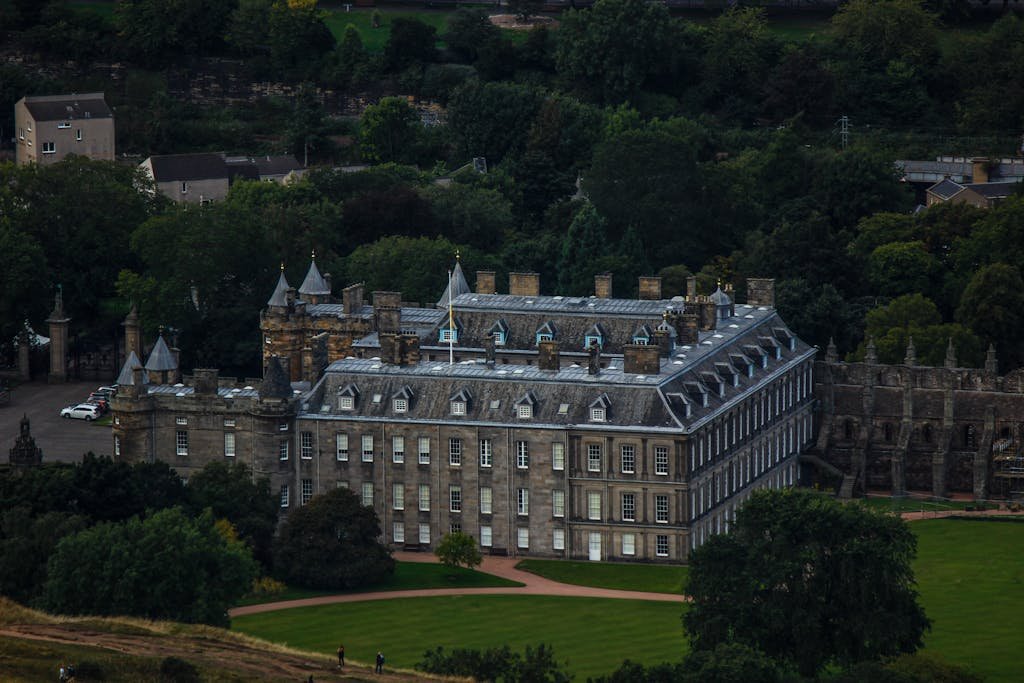 45 Unique Things to Do in Edinburgh: Hidden Spots & Must-See Attractions 5 Stunning aerial shot of the historic Palace of Holyroodhouse surrounded by lush greenery in Edinburgh, Scotland.
