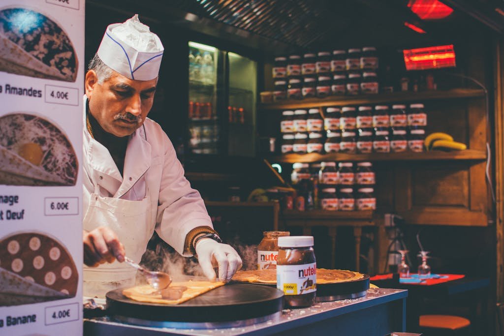 A chef skillfully prepares a Nutella crepe in a cozy Parisian café. Indoor ambiance and culinary expertise.