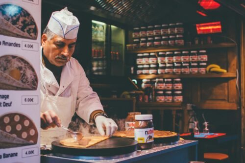 A chef skillfully prepares a Nutella crepe in a cozy Parisian café. Indoor ambiance and culinary expertise.
