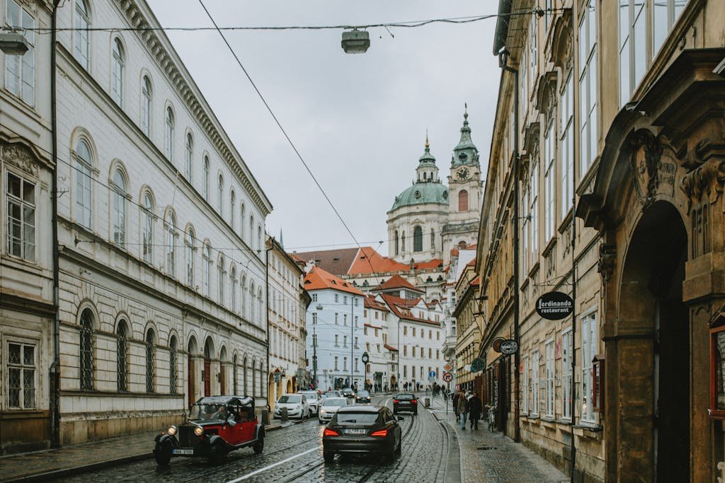3 Magical Days in Prague (My Prague travel Itinerary) 10 Charming street view showcasing historic architecture in Prague, features classic cars and bustling city life.