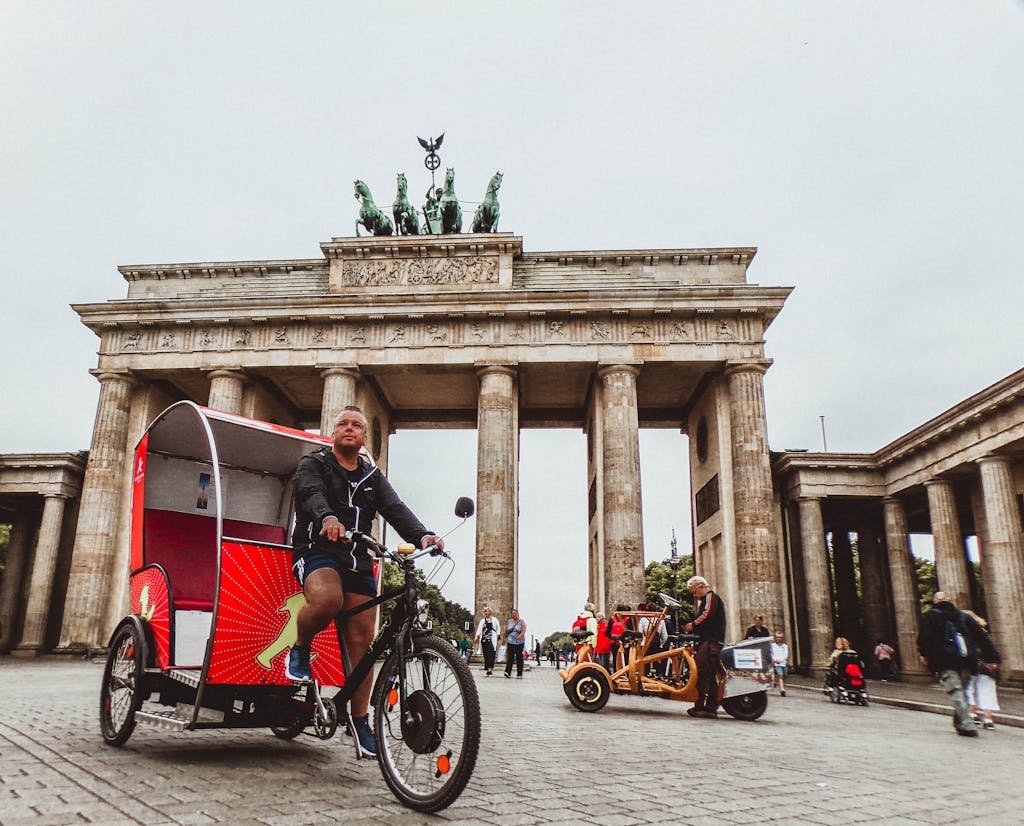 Rickshaw riders in front of the iconic Brandenburg Gate in Berlin, a popular tourist attraction.