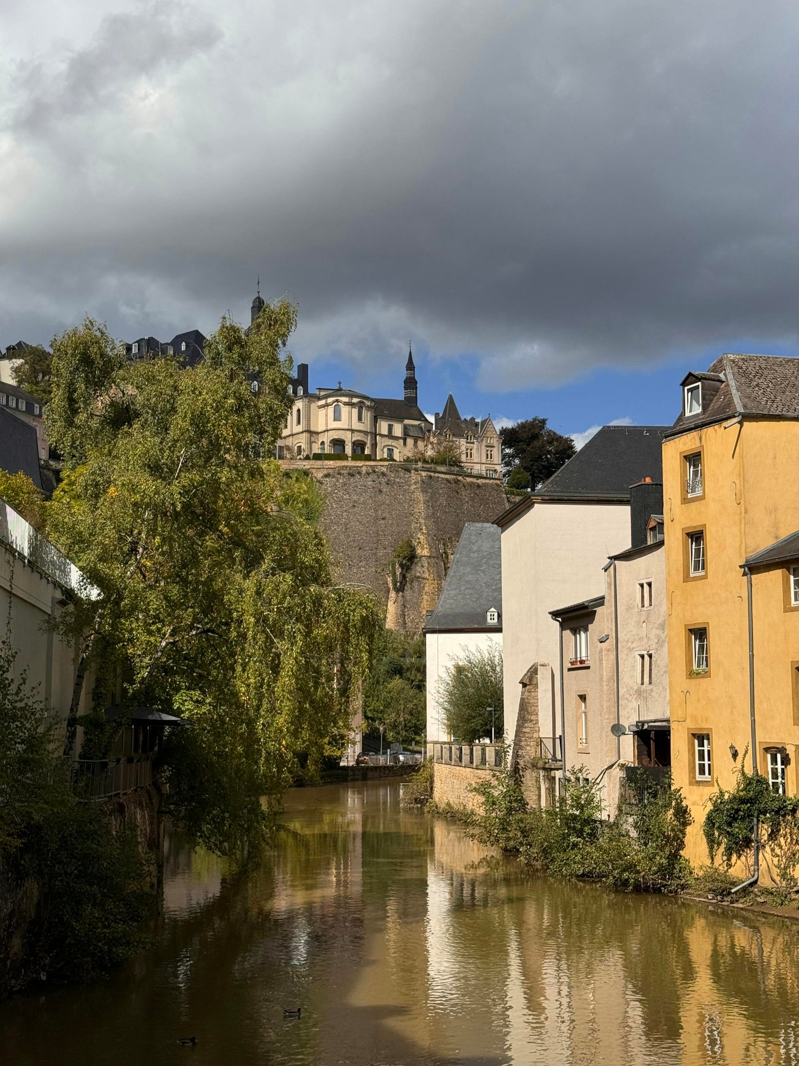 A picturesque view of Luxembourg's medieval city walls and Alzette River under a dramatic sky.