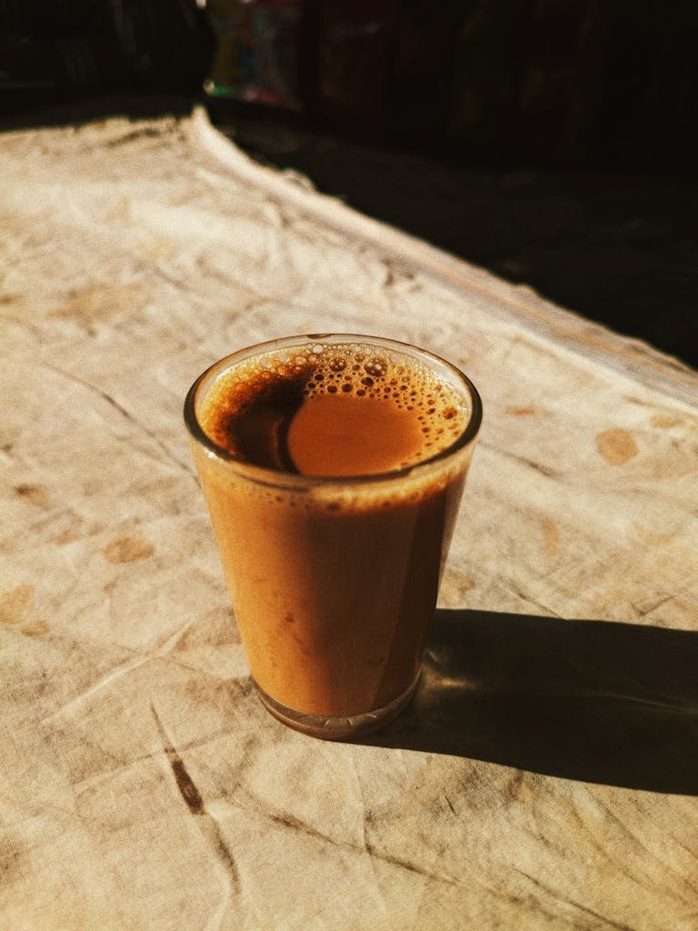 A steaming glass of masala chai casting a long shadow in warm sunlight on a rustic cloth surface.