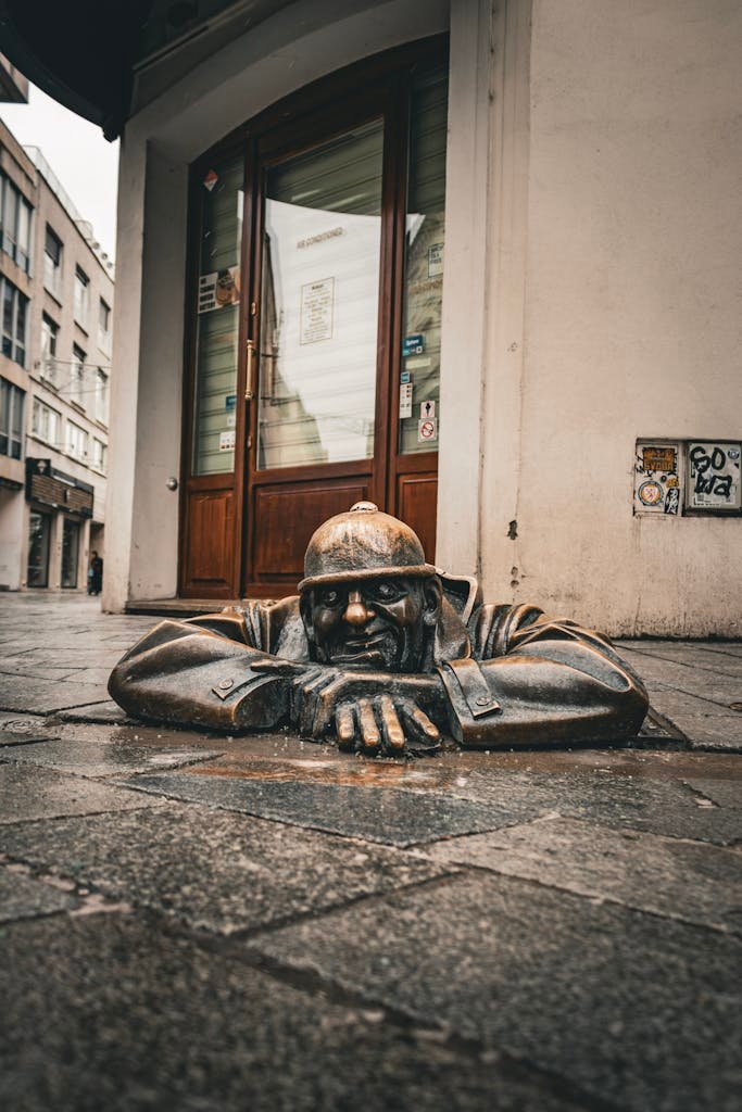 Bronze sculpture of a man emerging from a manhole on a paved city street, a unique urban attraction.