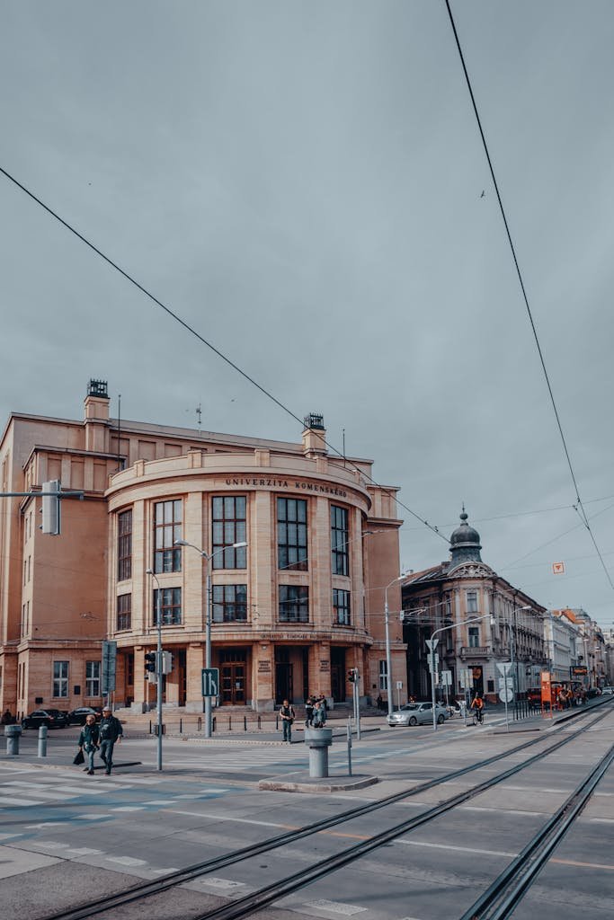 Street view of a historic building in Bratislava, featuring tram lines and people walking.