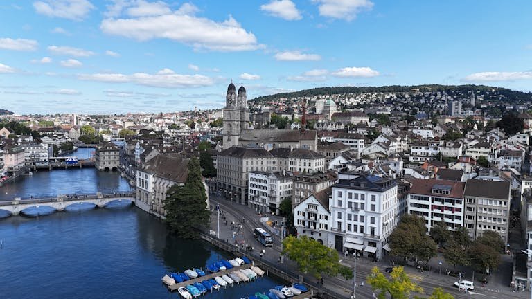 16 Amazing Things to Do in Zurich for First-Time Visitors 7 Aerial cityscape of Zurich, showcasing historic architecture, river, and Limmatquai under a vibrant blue sky.
