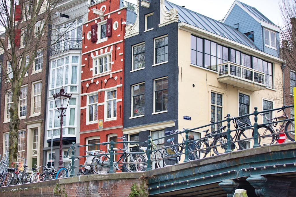 Bicycles lined along a bridge in Amsterdam with historic buildings in the backdrop, showcasing city charm.