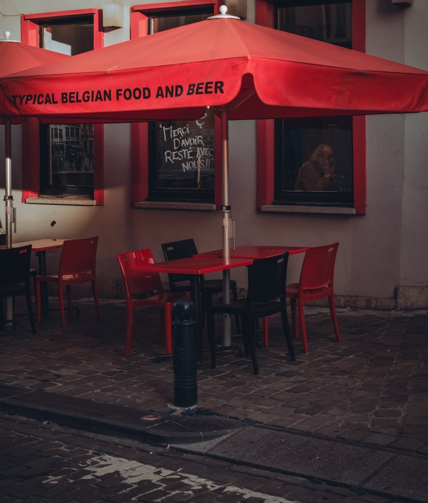 15 Best Things To Do In Brussels Belgium: Tips for first time visitors 16 Charming outdoor Belgian cafe with red umbrella and tables in a quaint old town setting.