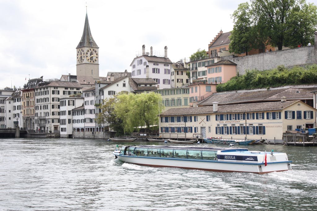 How to Spend the Perfect 5 Days in Switzerland Itinerary? 20 Charming riverside view in Zurich with a modern boat on Limmat River and historic architecture in the background.