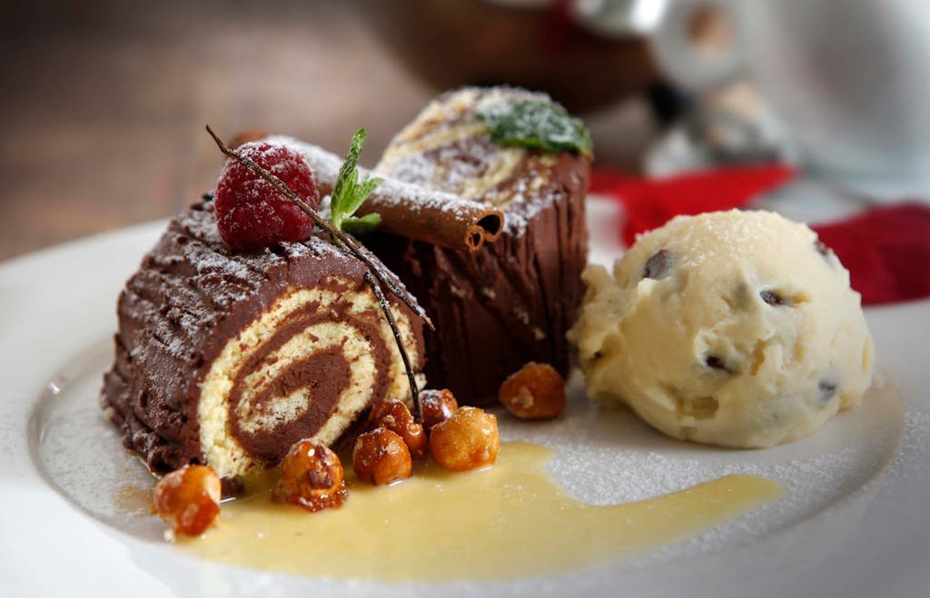 How to Spend the Perfect 5 Days in Switzerland Itinerary? 21 Delicious chocolate Swiss roll served with vanilla ice cream and candied nuts on a ceramic plate.