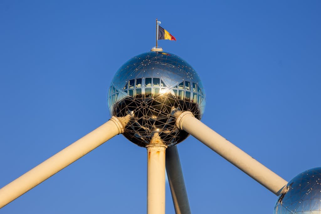 15 Best Things To Do In Brussels Belgium: Tips for first time visitors 11 Iconic Atomium structure with Belgian flag in Brussels, showcasing modern design and metal architecture.