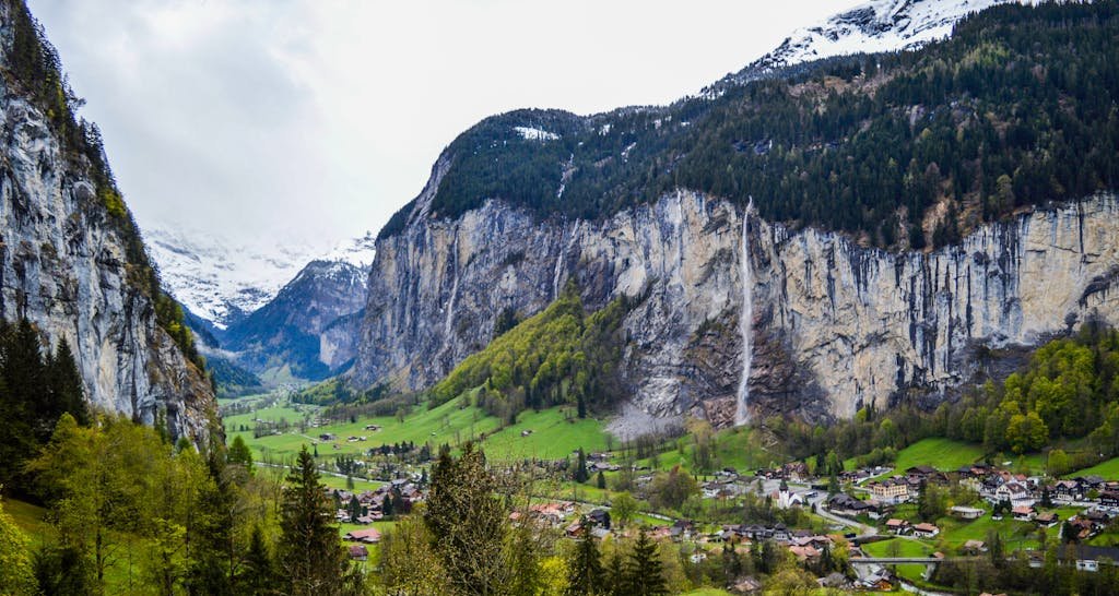 How to Spend the Perfect 5 Days in Switzerland Itinerary? 14 Magnificent alpine landscape of small Lauterbrunnen village located on grassy terrain between snowy rocky mountains and waterfall against cloudy sky in Switzerland