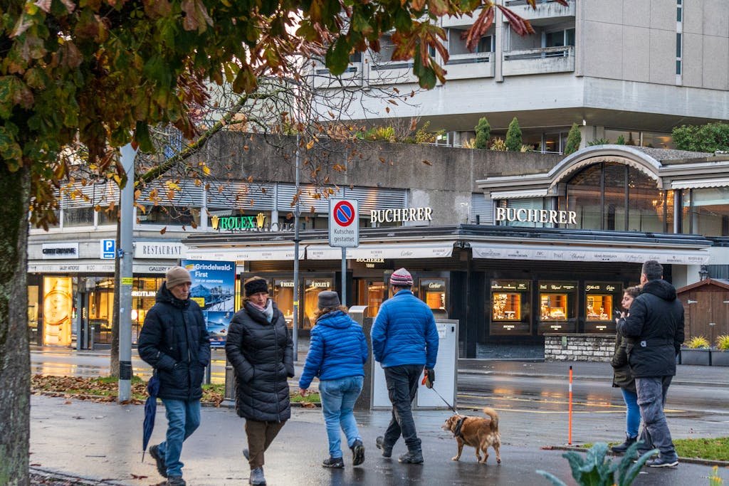 How to Spend the Perfect 5 Days in Switzerland Itinerary? 9 People enjoying a crisp autumn walk in Interlaken, Switzerland, lively streetscape with Bucherer store.
