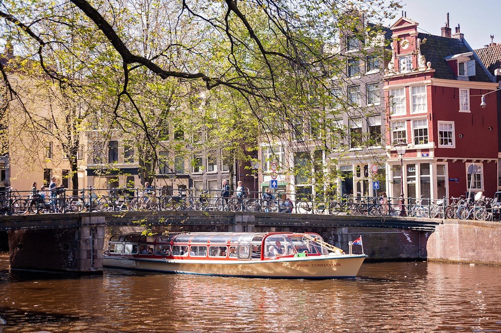 9 Ways of Getting Around Amsterdam Like a Local 6 Picturesque Amsterdam canal view featuring a tour boat passing under a classic Dutch bridge getting around amsterdam