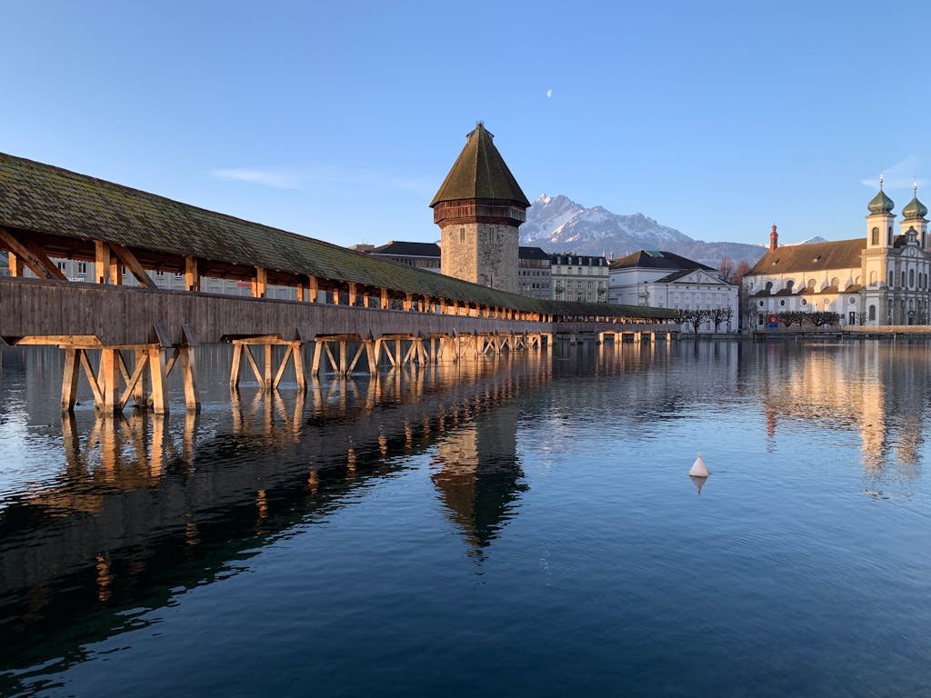 How to Spend the Perfect 5 Days in Switzerland Itinerary? 8 Picturesque scenery of famous ancient Chapel Bridge with water tower crossing river against cloudless blue sky in Lucerne