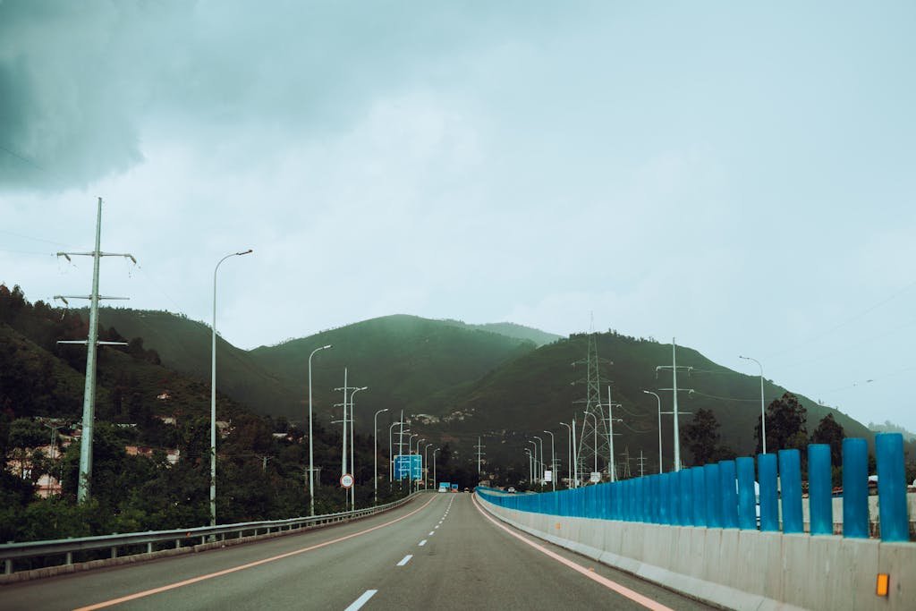 A picturesque highway leading through lush green mountains under a cloudy sky, ideal for travel themes.