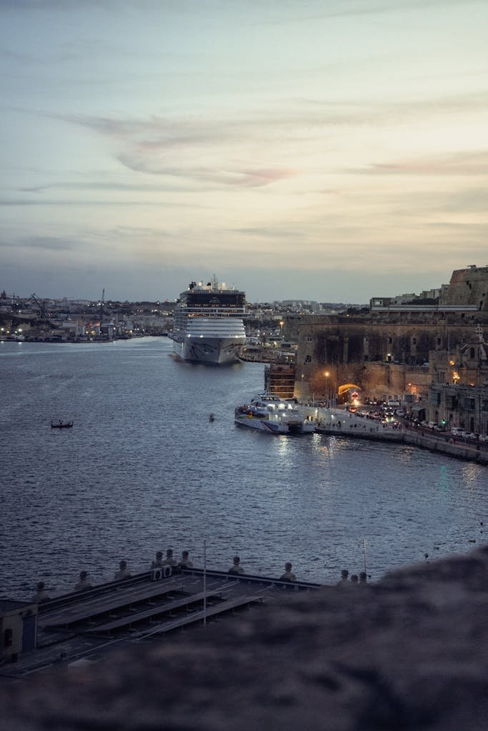 A scenic view of a cruise ship entering the harbor in Valletta, Malta at twilight.