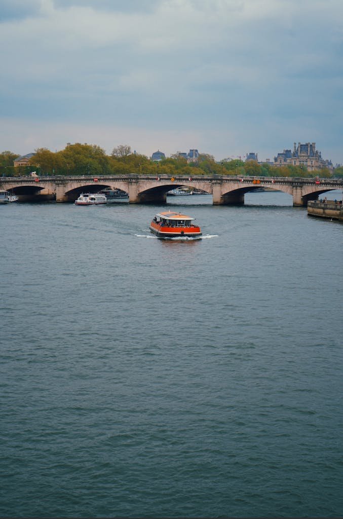 41 best Things to Do in Paris: Iconic Sights to Hidden Gems 8 A vibrant riverboat cruises the Seine under a historic bridge in Paris's serene atmosphere.