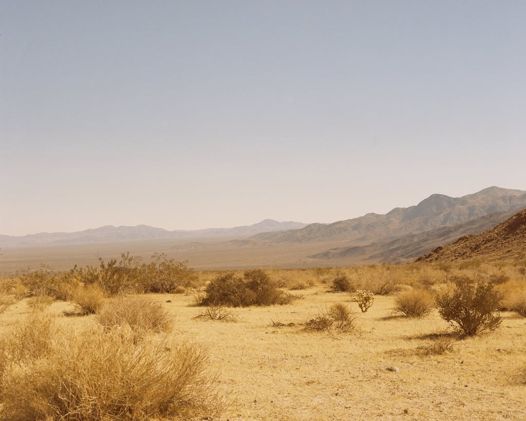 A wide view of a barren desert landscape with mountains in the distance under a clear sky.