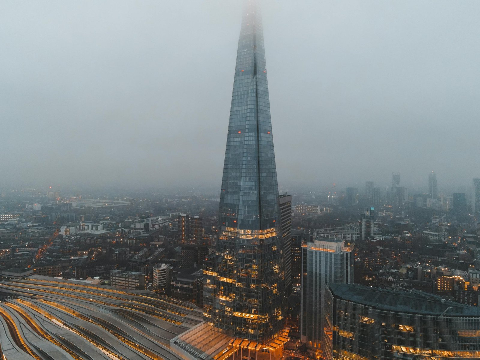 Aerial view of London city located in England with modern buildings and Shard skyscraper near railroads under gray cloudy sky in hazy day in daytime