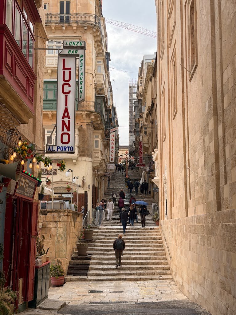 Bustling street in Valletta, Malta with tourists on iconic stairs. Historic charm and local vibe captured.