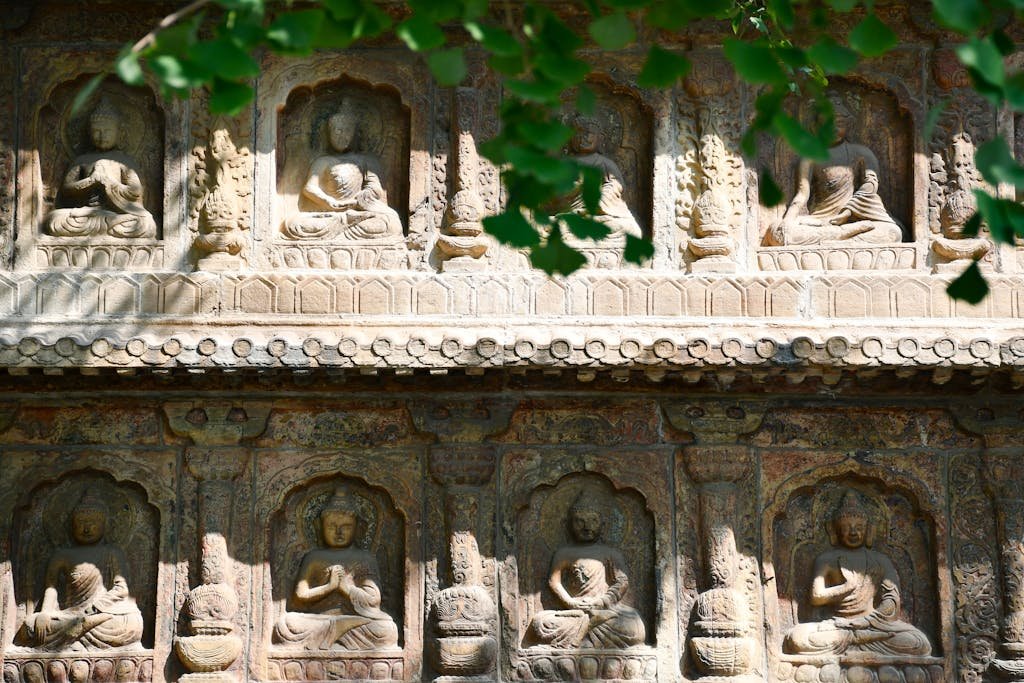 Detailed stone carvings of Buddha figures adorn an ancient temple facade, surrounded by nature.