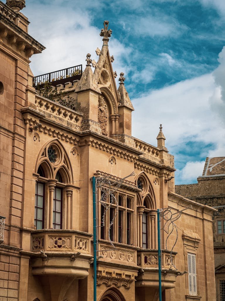 21 Best things to do in Mdina, Malta's Silent City 12 Elegant beige stone building with Gothic features in Rabat, Malta under a bright blue sky.