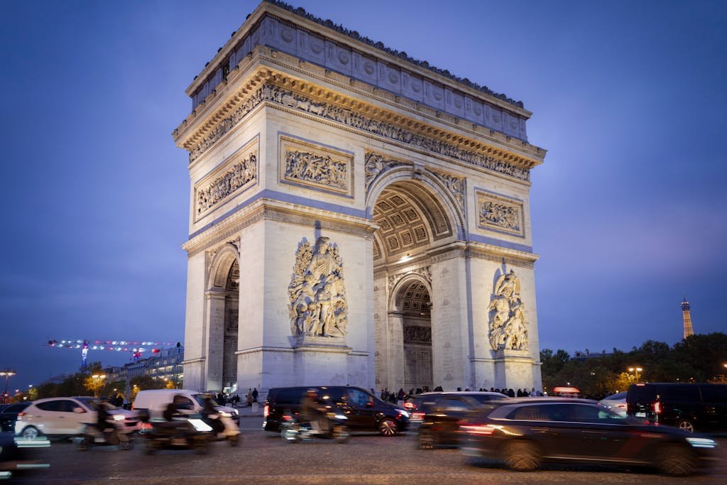 11 Ways For Getting Around Paris Efficiently: Ultimate guide 9 Iconic Arc de Triomphe under blue evening sky with bustling traffic in Paris.