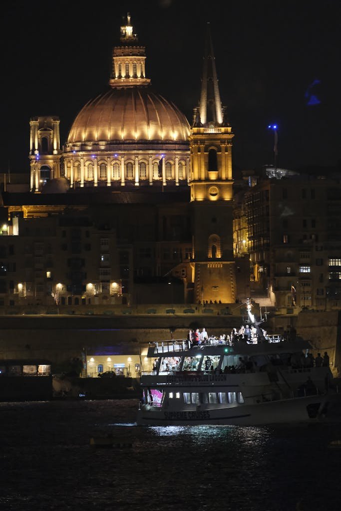 Night view of Valletta, Malta featuring the illuminated Saint Paul's Cathedral with a boat in the foreground.