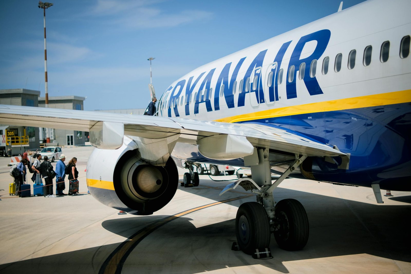 Passengers boarding a Ryanair plane on a sunny day at a Sicilian airport.