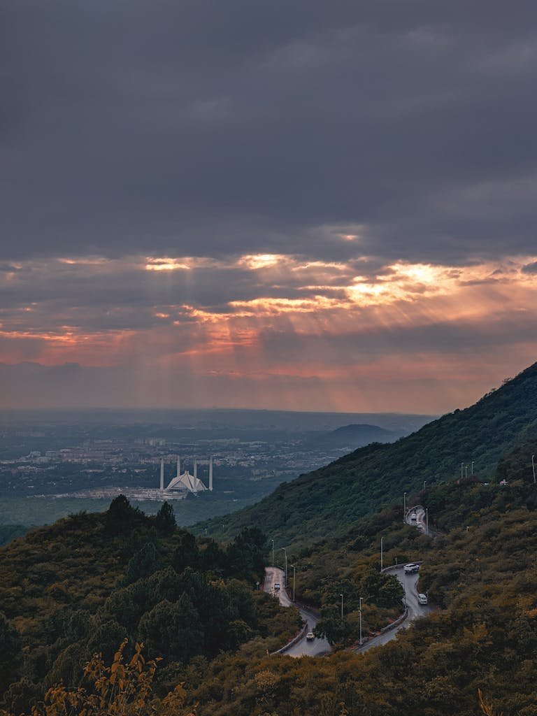 Scenic view of Faisal Mosque in Islamabad under a dramatic sunset with mountainous backdrop.