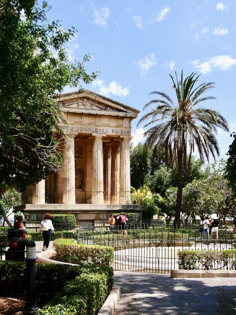 Stunning neoclassical temple surrounded by lush foliage and visitors in Valletta, Malta.