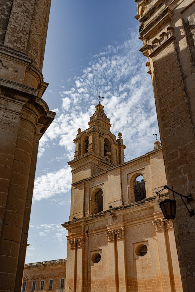 21 Best things to do in Mdina, Malta's Silent City 10 Sunlit stone architecture of an ancient Maltese church with a blue sky backdrop.